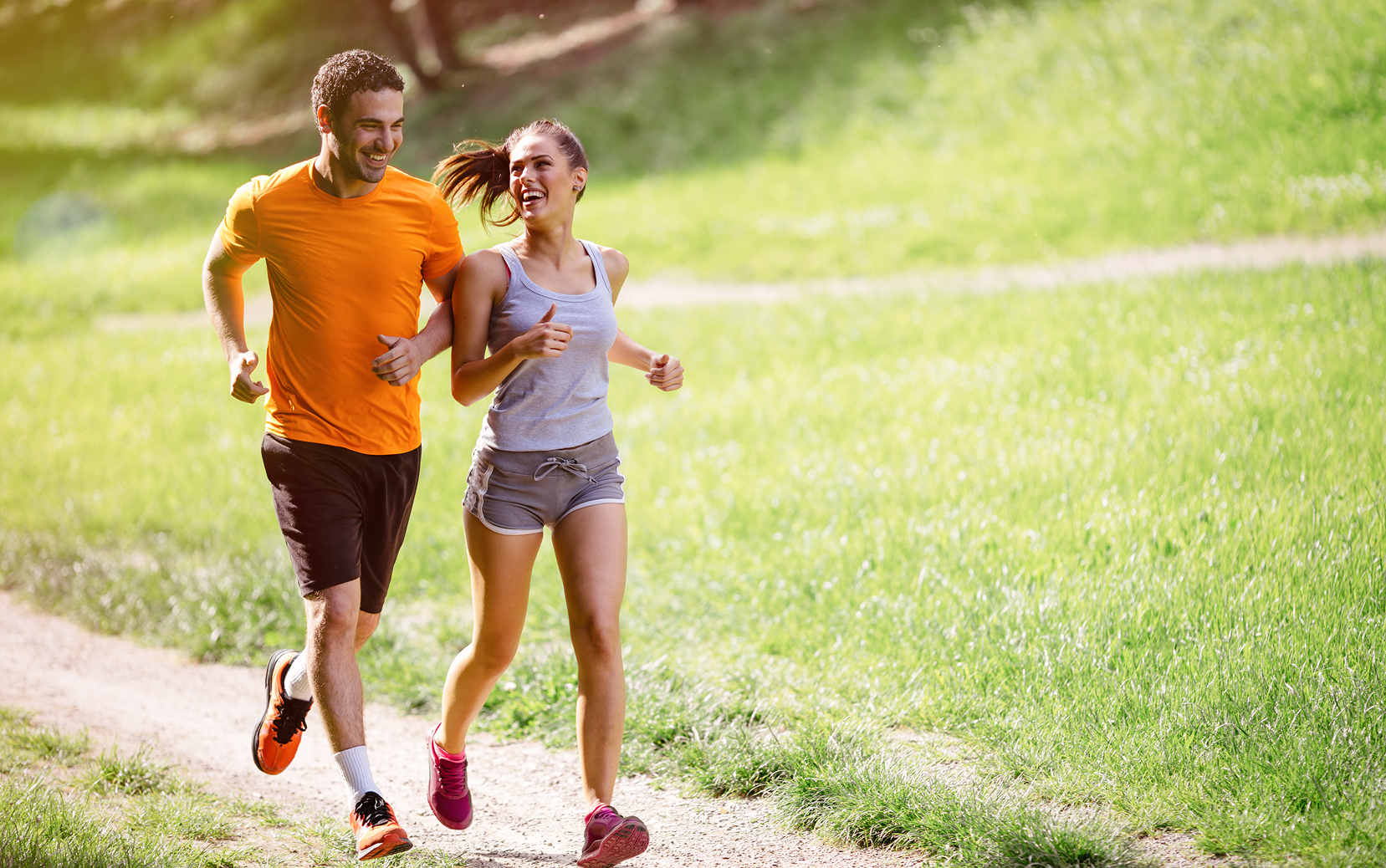 Imagem de fundo com um homem e uma mulher correndo juntos em um caminho ao ar livre, sorrindo e aparentando bem-estar, em um ambiente verde e ensolarado.